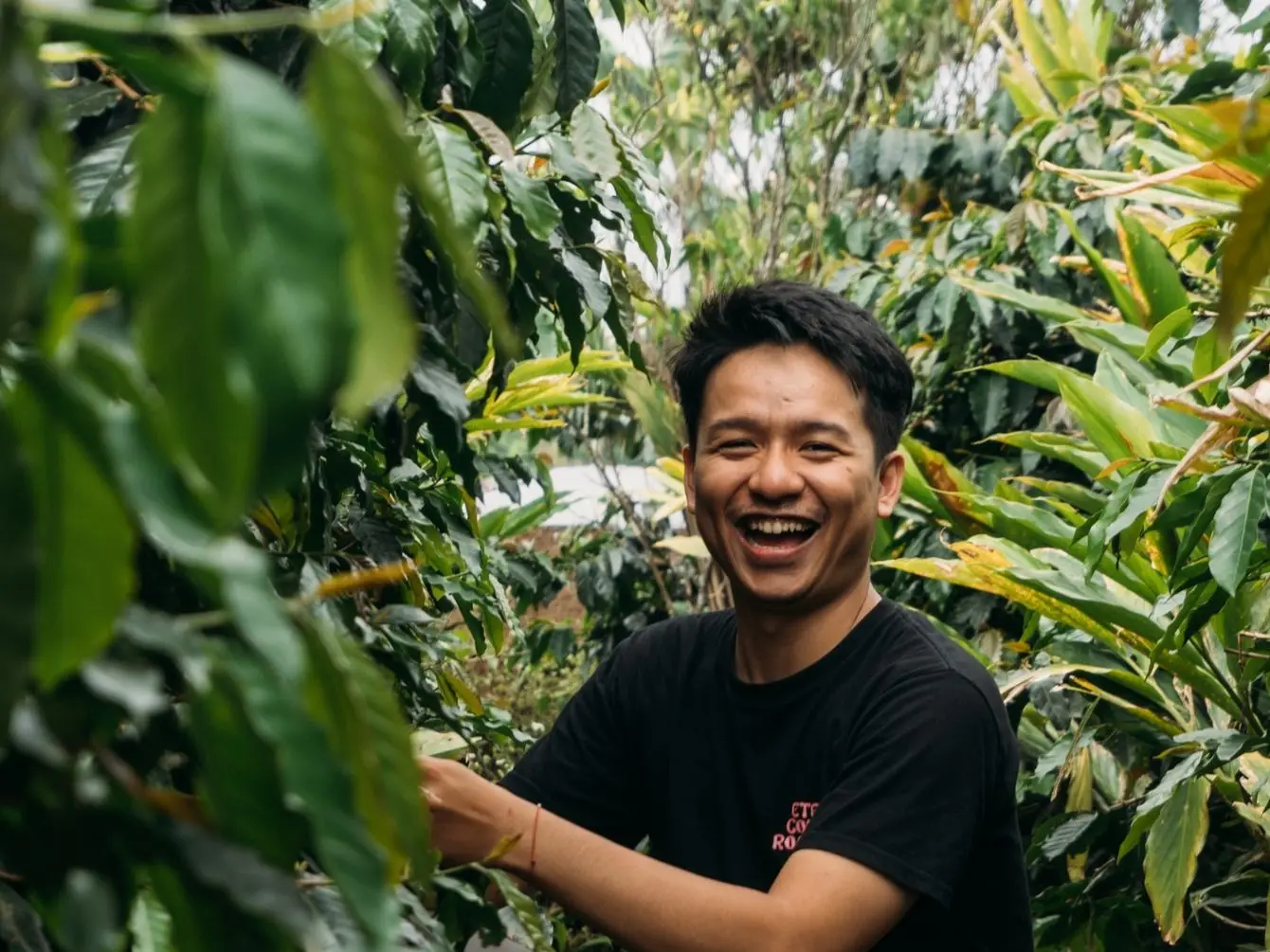 Petani kopi mitra TANDUR tersenyum di antara tanaman kopi